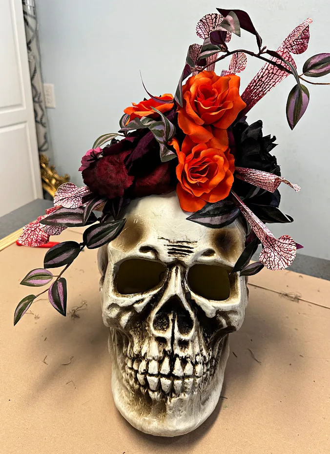 Faux skull surrounded by dark red and black flowers in a low bowl