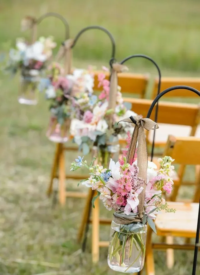 Metal shepherd hooks beside aisle chairs holding small hanging flower bunches
