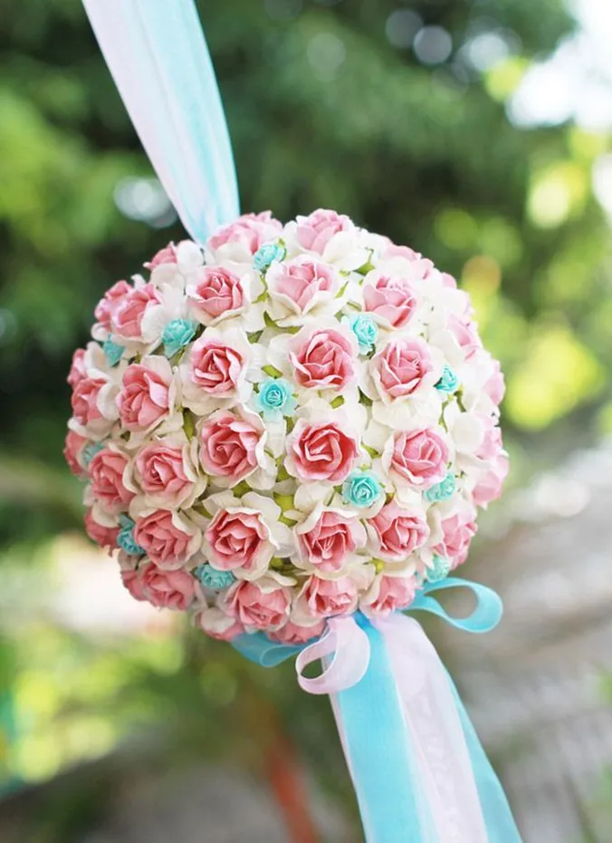 Round flower pomander balls hanging from ribbons beside a wedding aisle