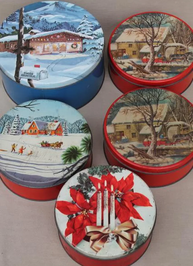 Stack of vintage Christmas cookie tins with snowy village scenes on a kitchen counter