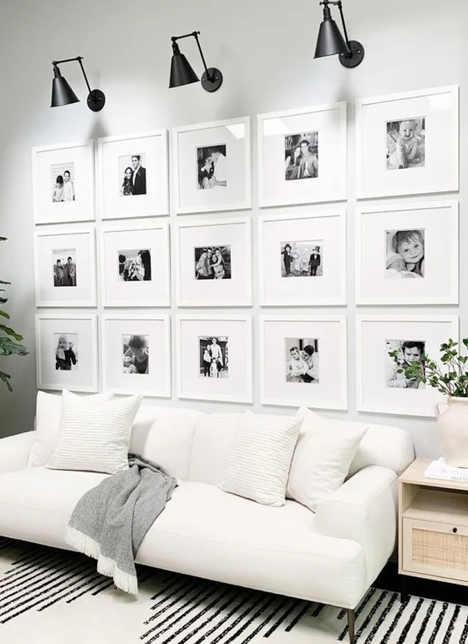 Symmetrical grid of white framed family photos hung above a white sofa