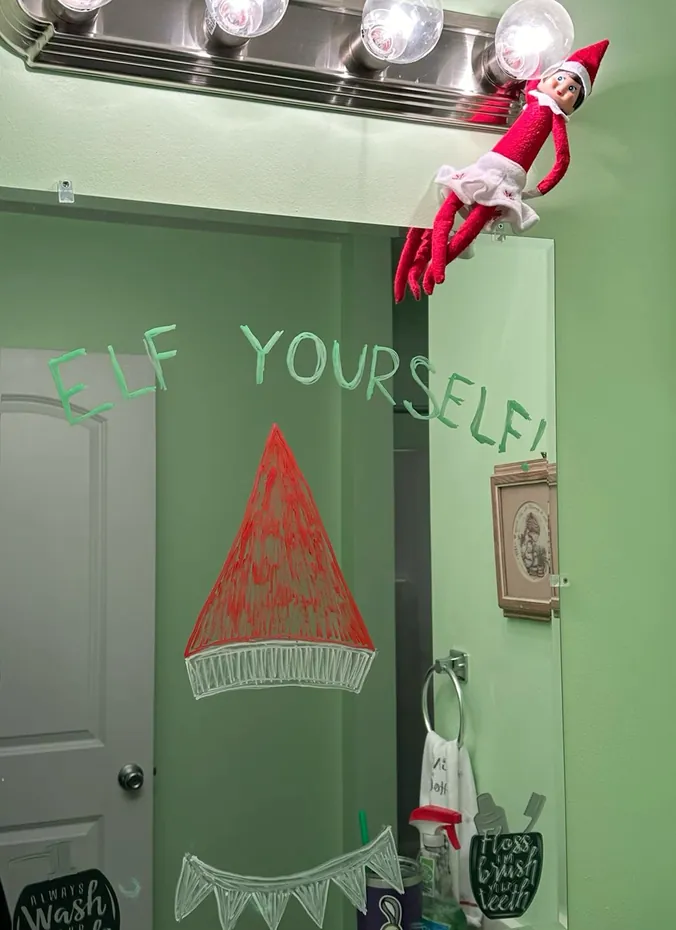 Elf on the shelf next to a funny message written on a bathroom mirror