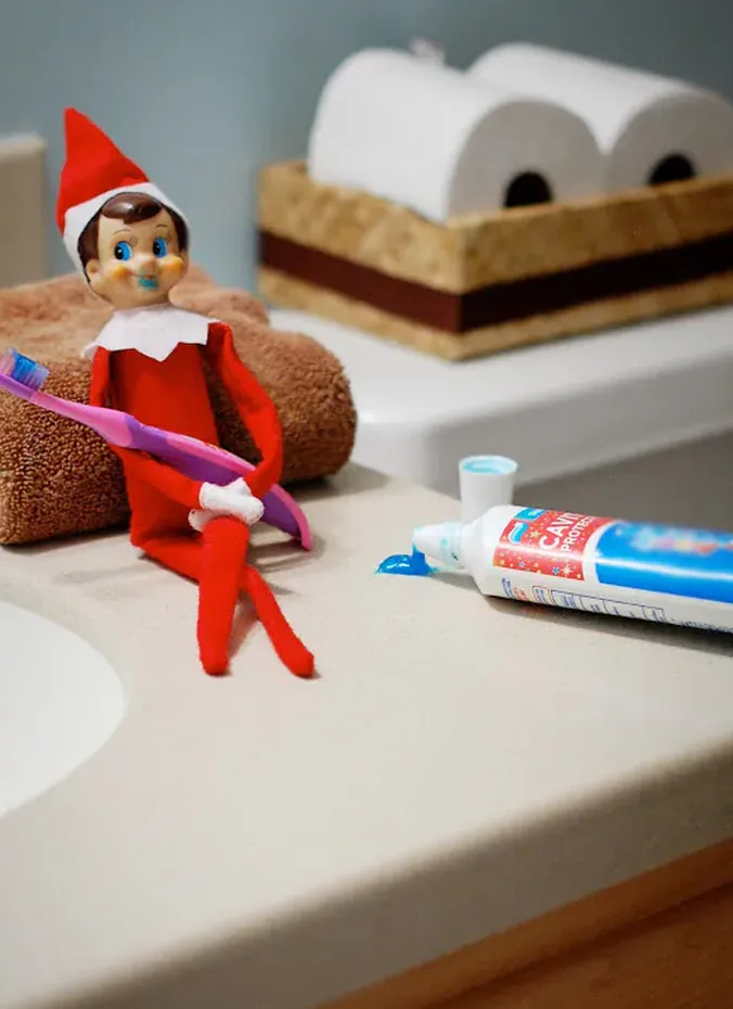 Elf on the shelf brushing teeth with toothpaste by the bathroom sink