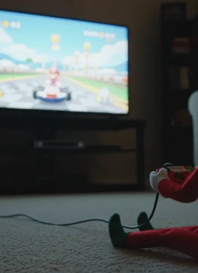 Elf on the shelf holding a video game controller on the couch