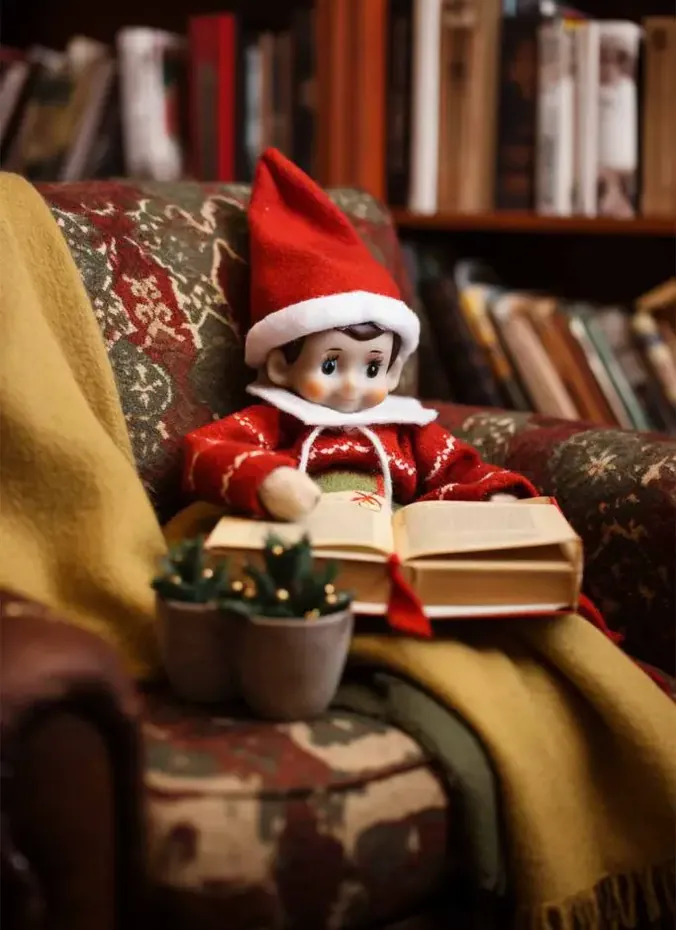 Elf on the shelf reading a tiny book in a cozy blanket nook