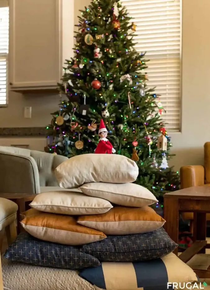 Elf on the shelf sitting on top of a tall pillow tower
