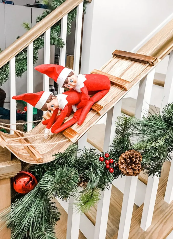 Elves on the shelf sledding down the stairs on a wooden sled