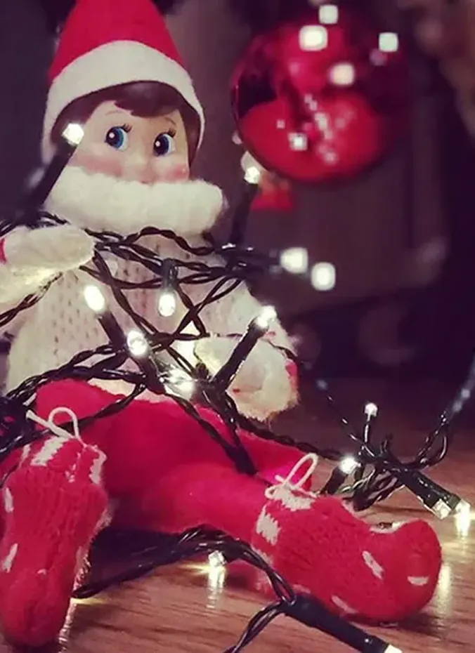 Elf on the shelf tangled in glowing Christmas fairy lights