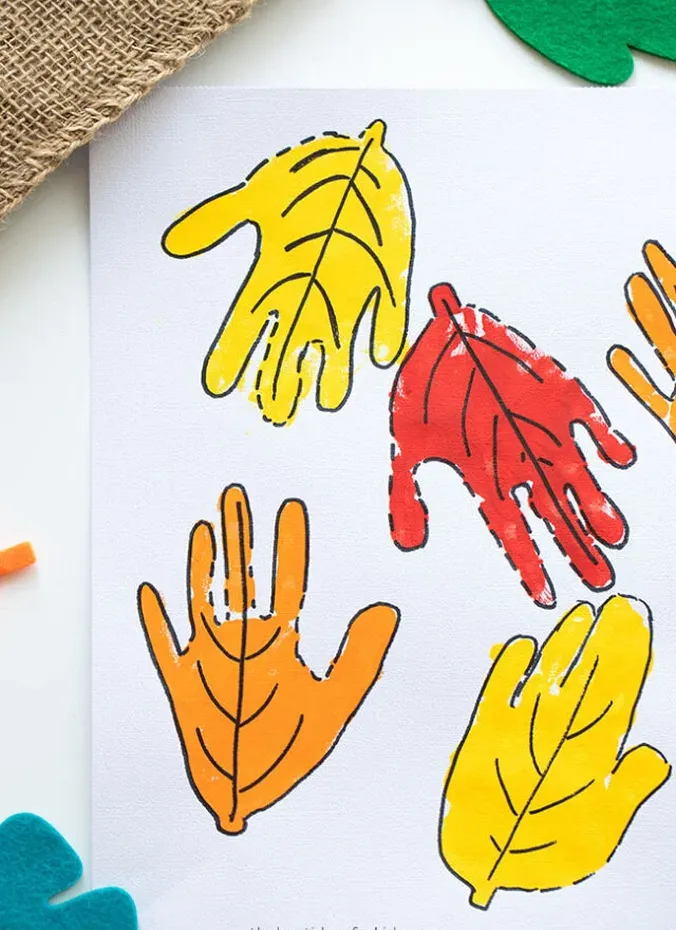 Child handprints painted in fall colors to look like autumn leaves on white paper