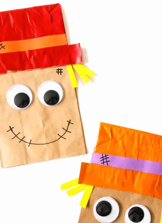 Paper bag scarecrow puppets with red hats and googly eyes made by kids