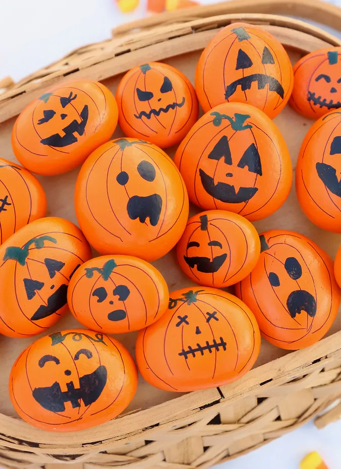 Rocks painted as orange pumpkins with jack o lantern faces in a basket