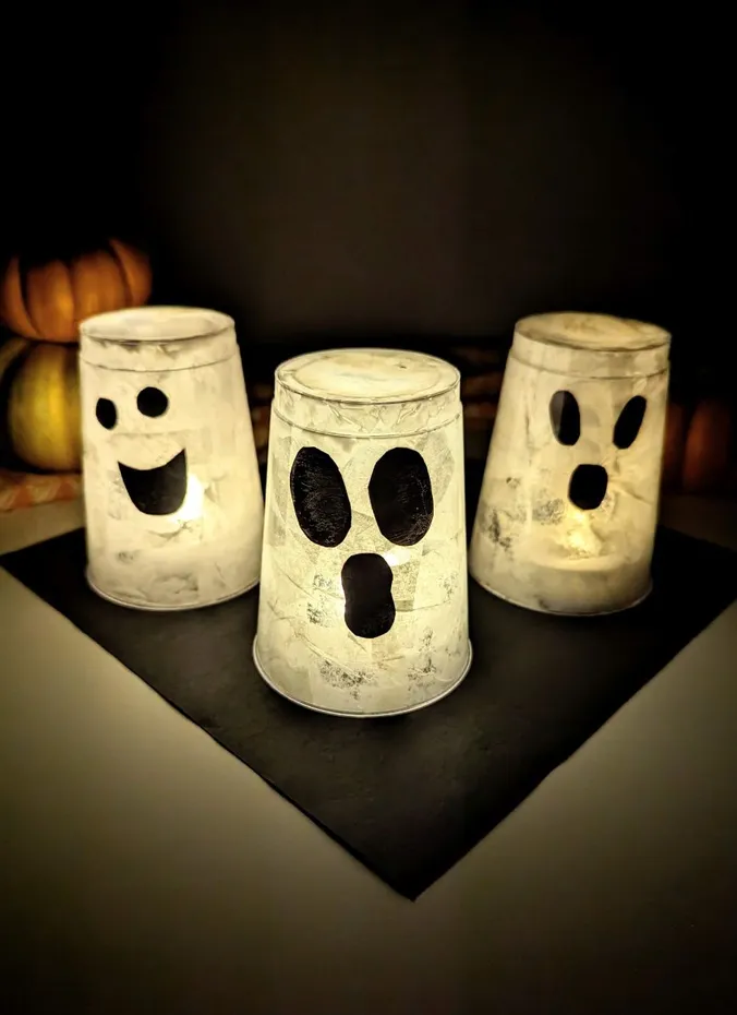 Glowing paper cup ghost lanterns with cute faces on a table
