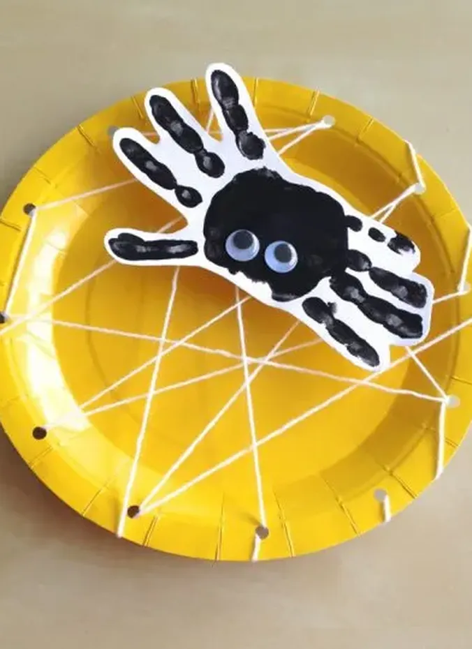 Handprint spider craft with googly eyes on a yarn paper plate web