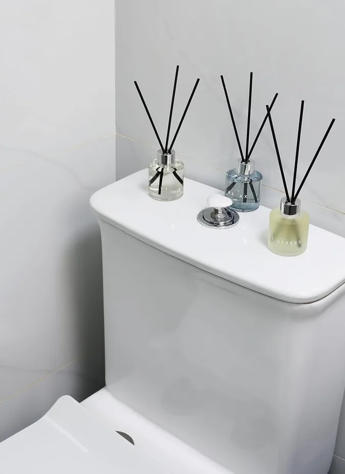 Reed diffuser in a glass bottle on a toilet tank in a bathroom